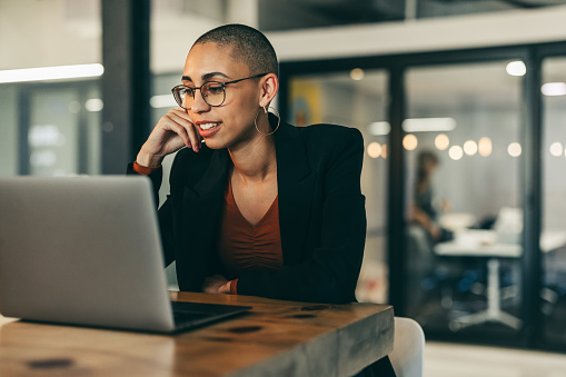 Young businesswoman attending a virtual meeting in a modern office. Confident young businesswoman using a laptop for a video conference with her global partners. Businesswoman sitting at her office desk.