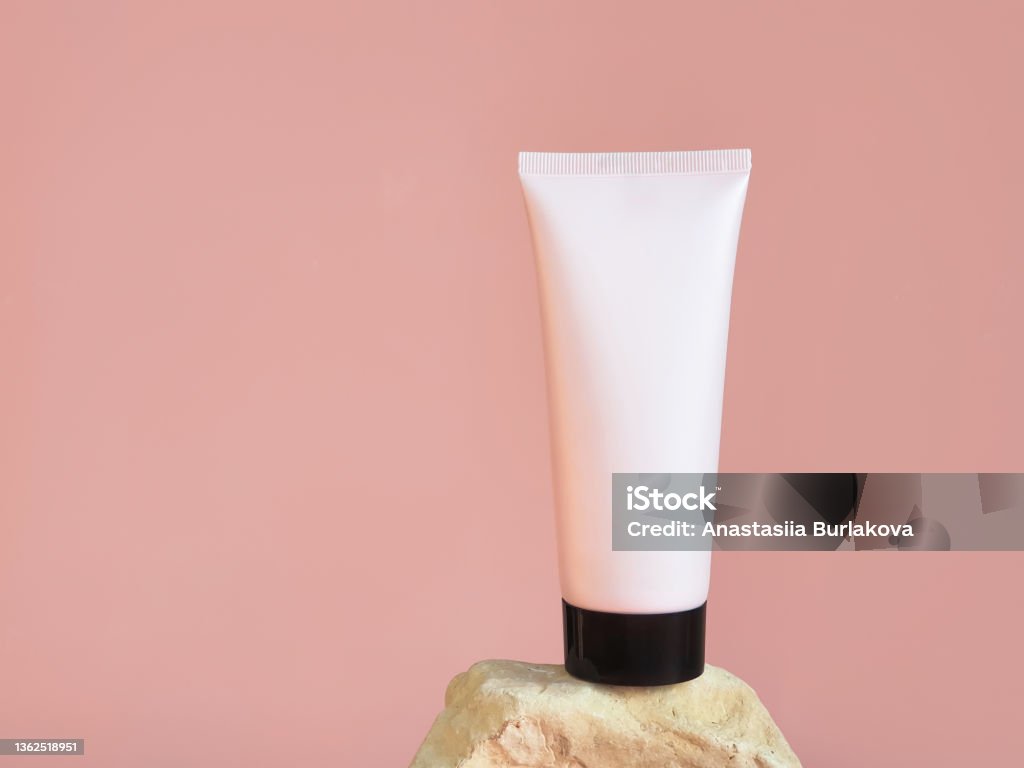 Unbranded pink squeeze cosmetic plastic tube with black cap on rock isolated on pink background. Bottle for branding and label - moisturizer cream, gel, skin care, toothpaste, lotion, balsam. Mockup Advertisement Stock Photo