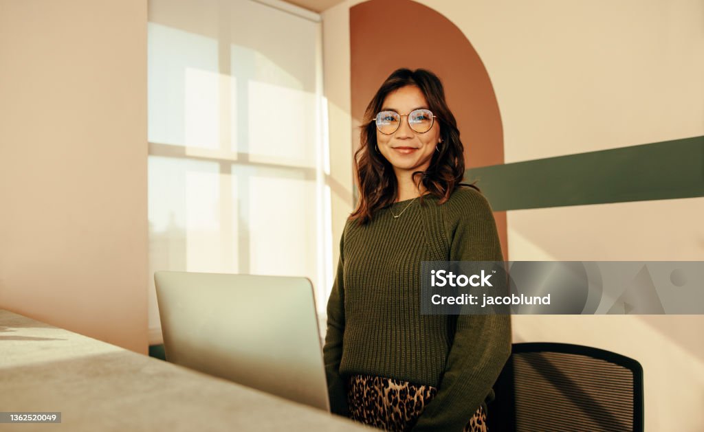 Cheerful receptionist standing at the front desk Cheerful receptionist standing at the front desk of a co-working space. Friendly female assistant looking at the camera while working at the reception in a modern office. Hotel Reception Stock Photo