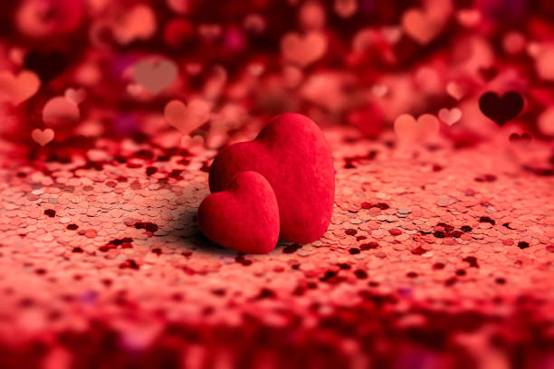 the symbol of love is two red hearts side by side on a red background of hearts and lights out of focus. For valentine lovers or wedding layout stock photo