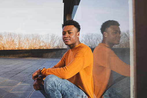 Young afro-american man wearing orange sweater reflected in a glass surface. City life concept.
