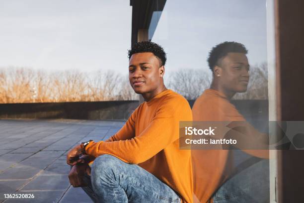 Young Afroamerican Man Wearing Orange Sweater Reflected In A Glass Surface Stock Photo - Download Image Now