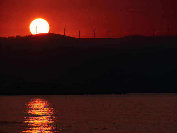 paysage pittoresque de moulins à vent modernes placés sur la colline sur fond d’un énorme soleil orange et d’un ciel couché le soir - dramatic sky dusk night sustainable resources photos et images de collection