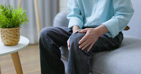 close up of asian elder man holding his knee and suffering joint pain at home