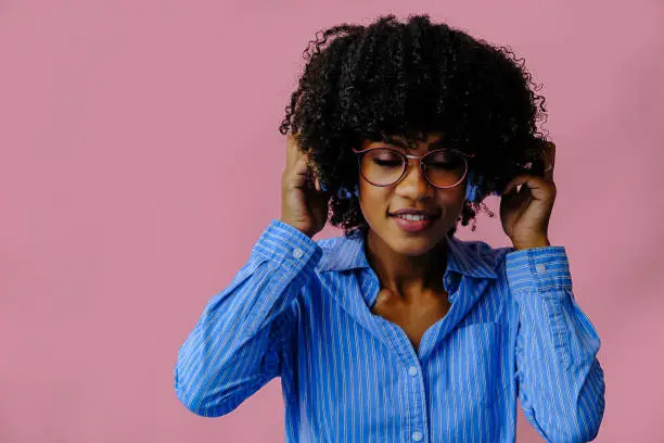 beautiful young African american woman listening music in headphones isolated on pink background