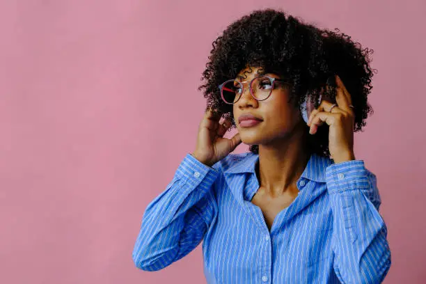 beautiful young African american woman listening music in headphones isolated on pink background