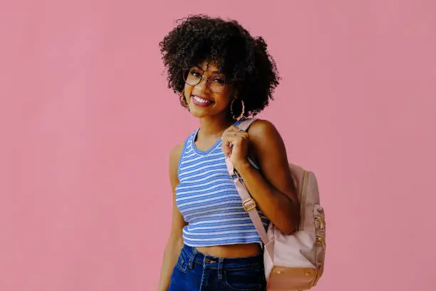 Photo of attractive girl in eyeglasses with backpack posing on pink background, back to school concept