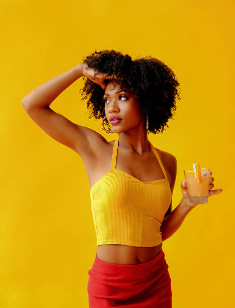 hermosa joven afroamericana con un brillante atuendo de verano bebiendo un refrescante cóctel aislado sobre fondo amarillo - women fashion summer fashion model fotografías e imágenes de stock