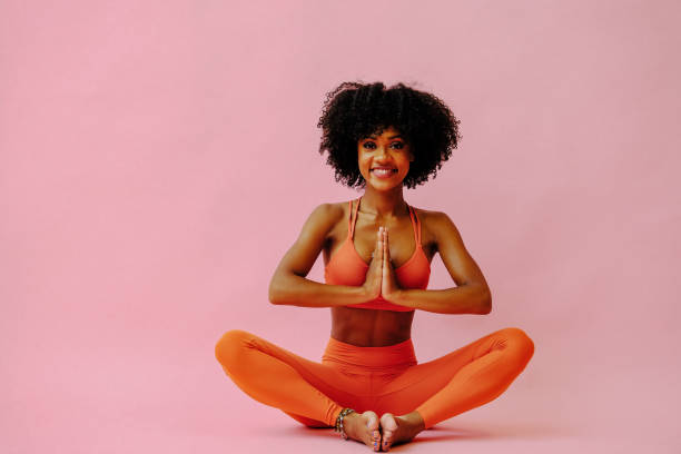 beautiful African american woman meditating in sports outfit on pink background beautiful African american woman meditating in sports outfit on pink background yoga instructor stock pictures, royalty-free photos & images