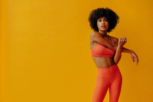 привлекательная молодая подтянутая женщина в спортивной одежде, растягивающаяся изолированно на оранжевом фоне - healthy style стоковые фото и изображения