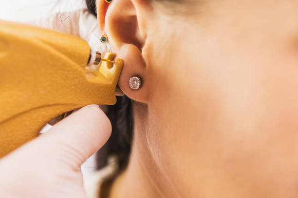 un médico con guantes médicos blancos estériles perfora las orejas de una niña en el consultorio médico con una pistola perforante. - piercings en el ombligo fotografías e imágenes de stock