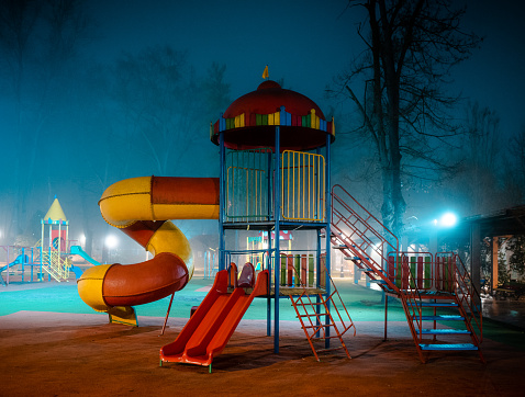 Atmospheric color image depicting a kids' playground shrouded in mist at night.