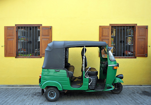 Tricycle autorickshaw 'tut-tut' parked outside colourful yellow ochre painted building, Galle, Sri Lanka, South Asia. Sri Lanka, formerly Ceylon, is a  beautiful warm tropical island off the south eastern coast of India with a rich history of Sinhalese kingdoms and a mixture of faiths including Hindu Buddhist and Tamil as well as Dutch and British colonial influences. It has a wealth of birdlife and wildlife including many endangered wild animals.