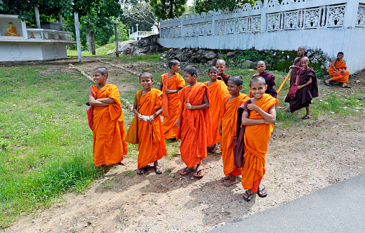 Buddhist novices in orange robes gather at the roadside, near Yala, Sri Lanka, South Asia. Sri Lanka, formerly Ceylon, is a  beautiful warm tropical island off the south eastern coast of India with a rich history of Sinhalese kingdoms and a mixture of faiths including Hindu Buddhist and Tamil as well as Dutch and British colonial influences. It has a wealth of birdlife and wildlife including many endangered wild animals.