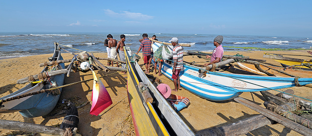 Kalutara beach fishermen discuss the day's catch around their outrigger fishing boats, Kalutara, or Kalutota, Sri Lanka, South Asia. Sri Lanka, formerly Ceylon, is a  beautiful warm tropical island off the south eastern coast of India with a rich history of Sinhalese kingdoms and a mixture of faiths including Hindu Buddhist and Tamil as well as Dutch and British colonial influences. It has a wealth of birdlife and wildlife including many endangered wild animals.