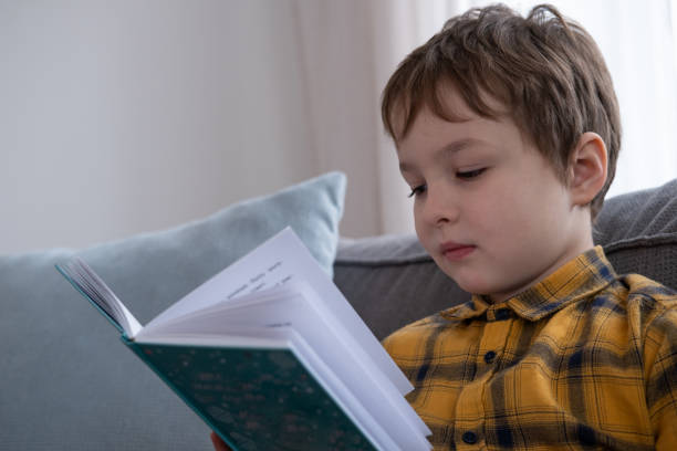 istock little boy sitting on the sofa and reading a book 1362538516