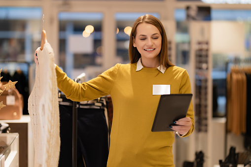 Young woman a clothing store manager sorting products and using a digital tablet at the workplace