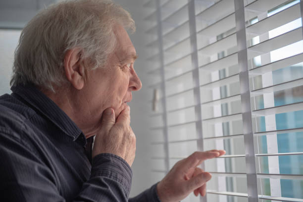 curioso hombre mayor mirando a la ventana - entrometido fotografías e imágenes de stock
