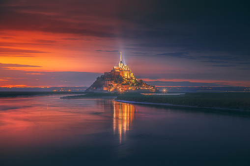 Beautiful view of famous Le Mont Saint Michel illuminated with city lights. East across the tidal bay from salt marsh at a beautiful sunrise time in Normandy, Northern France