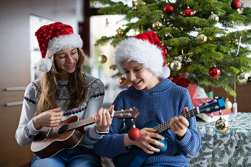 Brother and sister practicing playing Christmas carols on ukuleles.\nCanon R5