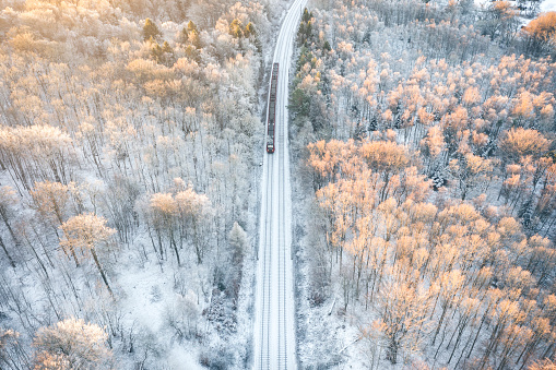 Electric city train running on rails through winter wonderland in a snow covered forest in Denmark. Aerial view shot with drone. Public transportation by train and bus are together with bicycling the fastest way to to get to work in this capital.