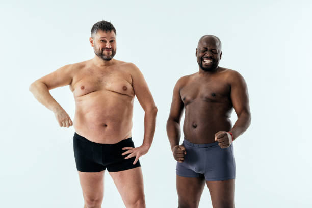 two multiethnic men posing for a male edition body positive beauty set. Shirtless guys with different age, and body wearing boxers underwear two multiethnic men posing for a male edition body positive beauty set. Shirtless guys with different age, and body wearing boxers underwear fat guy no shirt stock pictures, royalty-free photos & images