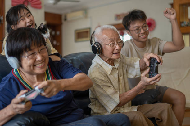 2 Asian Chinese grandparent playing video game at home with grandchildren. stock photo