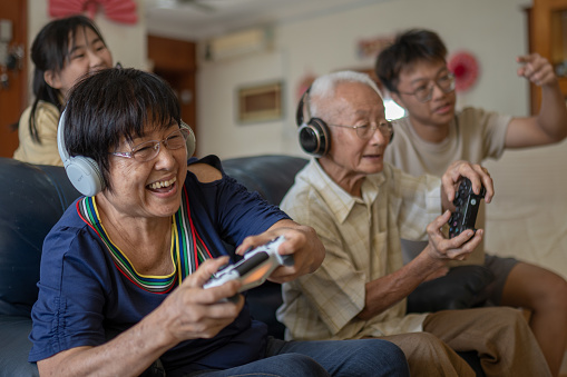 2 Asian Chinese grandparent playing video game at home with grandchildren.