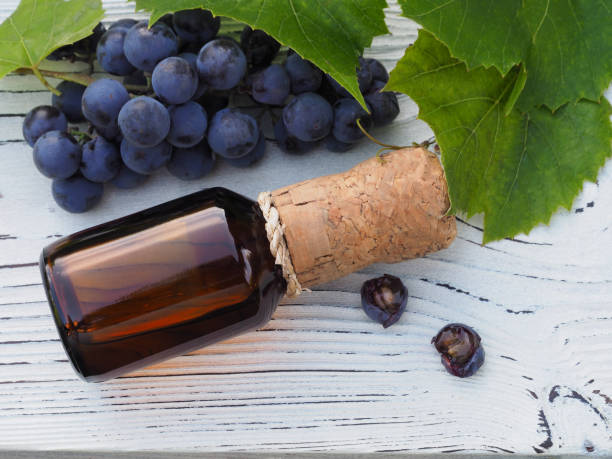 экстракт, масло в бутылке, спелый голубой виноград с зелеными лис�тьями на белом деревянном столе, плоская раскладка. косметический продукт  - wine cork antioxidant wineglass autumn стоковые фото и изображения