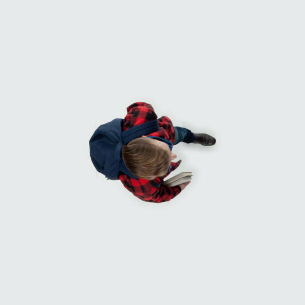 Generation z young male student walking in front of white background wearing backpack and holding textbook and using headphones