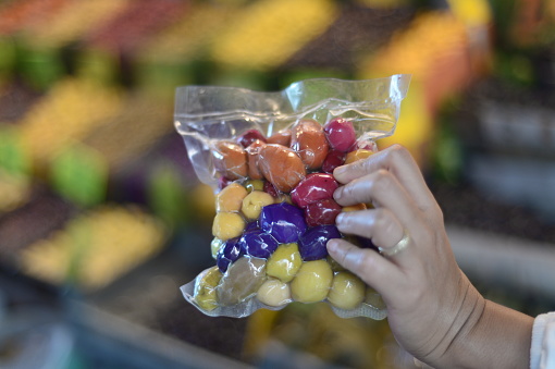 Hand holding colorful bag of green orange red and purple olives with beautiful colorful bokkeh background blur