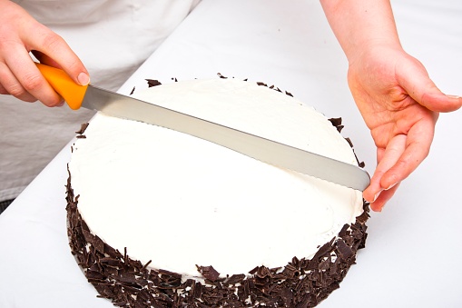 Confectioner marks the division of a Black Forest gateau with a cake knife so that there are exactly twelve pieces of the same size. With light pressure on the cake knife, an imprint is created in the cream that marks the exact division into ten parts. With light pressure on the cake knife, an imprint is created in the cream that marks the exact division into equal parts. This image is a part of a series, step by step preparation of a Black Forest gateaux.