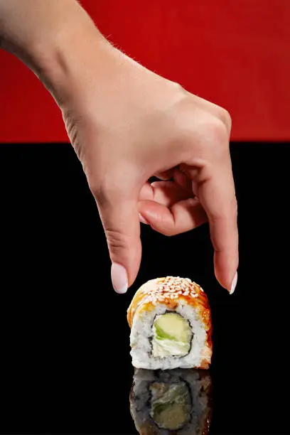 Photo of Female hand reaching out to unagi roll with eel, cream cheese