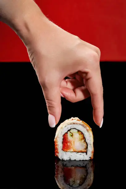 Photo of Female hand reaching out to roll with shrimp, tobiko, cucumber