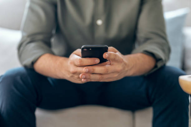 istock Hands of business man using smartphone texting while relaxing on sofa at home. 1362576915