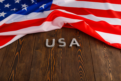 crumpled Unated States of America flag and with word USA laid with on flat textured wooden surface background in perspective view