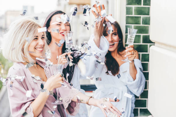 Pretty young women friends in bathrobes and pajama clink elegant glasses with delicious champagne at bachelorette party on hotel room terrace stock photo