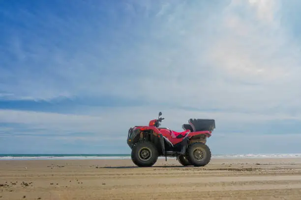 Low angle view of a red all-terrain quad bike standing on the sandy beach of Costa Rica at noon