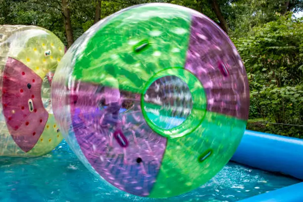 Photo of Water or aqua zorbing. Children play inside the inflatable transparent roller floating in swimming pool. Water walking or zorbing very popular fun activity and suitable for all ages.