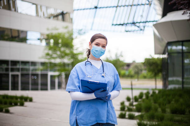 Portrait of positive and optimistic NHS medical staff in front of hospital Young female head of medical staff wearing blue uniform,frontline key worker specialist portrait in front of healthcare facility or nursing home clinic,positive and smiling,friendly face of optimism frontline worker mask stock pictures, royalty-free photos & images