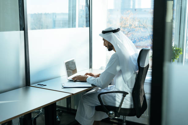 handsome man with traditional clothes working in an office of Dubai stock photo