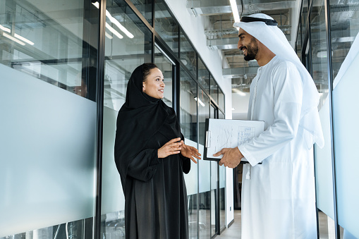 Man and woman with traditional clothes working in a business office of Dubai. Portraits of  successful entrepreneurs businessman and businesswoman in formal emirates outfits. Concept about middle eastern cultures, lifestyle and professional occupations