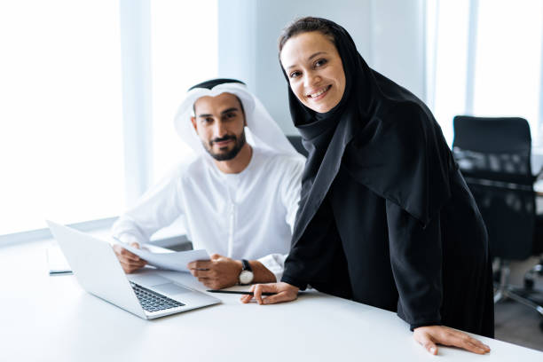 Handsome man and woman with traditional clothes working in an office of Dubai Man and woman with traditional clothes working in a business office of Dubai. Portraits of  successful entrepreneurs businessman and businesswoman in formal emirates outfits. Concept about middle eastern cultures, lifestyle and professional occupations emirati culture photos stock pictures, royalty-free photos & images