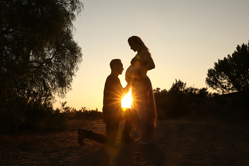 Silhouette of a pregnant woman and husband at sunset