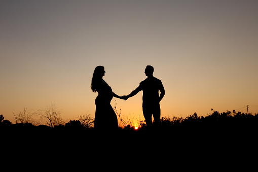 Silhouette of a pregnant woman and husband at sunset