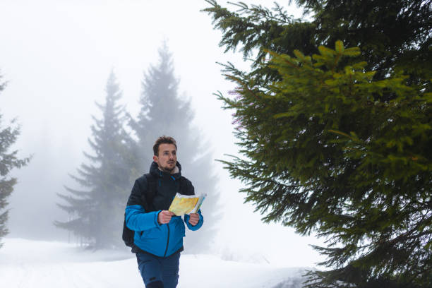 jeune randonneur en veste bleue perdu dans une montagne brumeuse et enneigée marchant sur un sentier tout en tenant une carte - trail marker hiking sign sports and fitness photos et images de collection