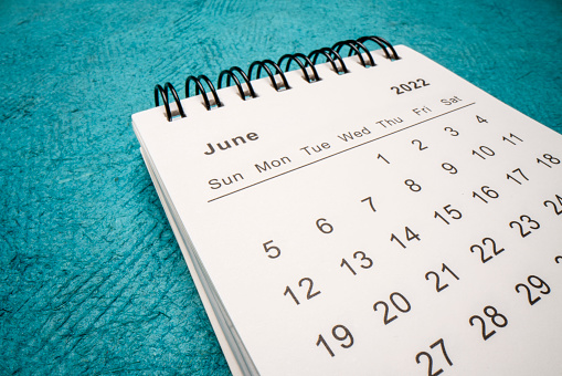 June 2022 - spiral desktop calendar against green handmade paper, low angle macro shot, time and business concept