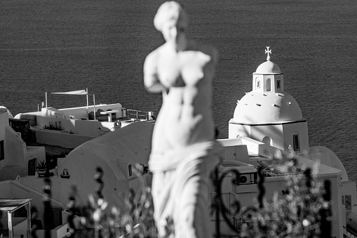 Church of St Minas in Firá on Santorini Caldera in South Aegean Islands, Greece, with a blurred garden ornament in the foreground.