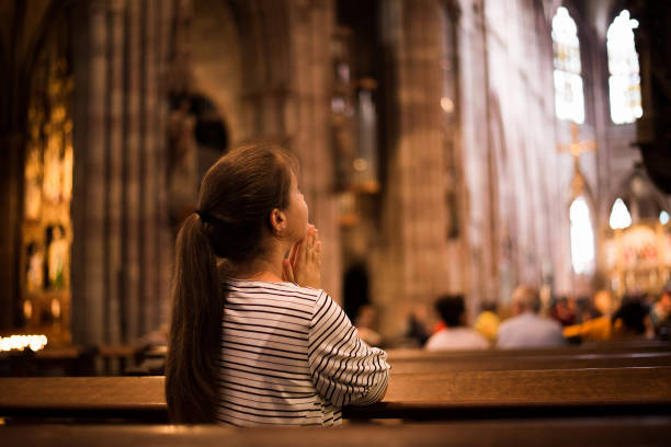 giovane ragazza che prega in chiesa in piedi sulle ginocchia - cattolicesimo foto e immagini stock