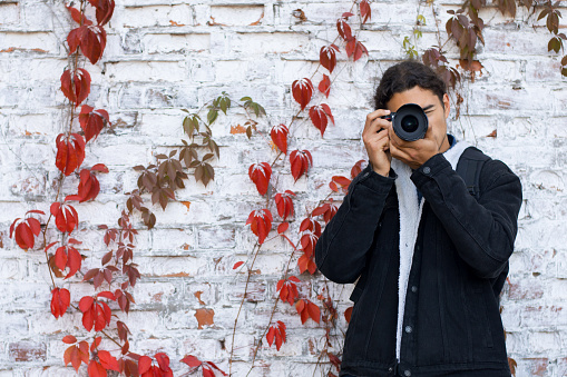 Young man standing near the white brick wall and taking pictures.